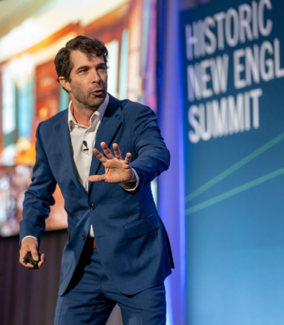 A photo of a male speaker in a suit at the 2024 Historic New England Summit.