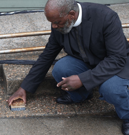 A man kneels to place a Stopping Stone memorial into a walkway.