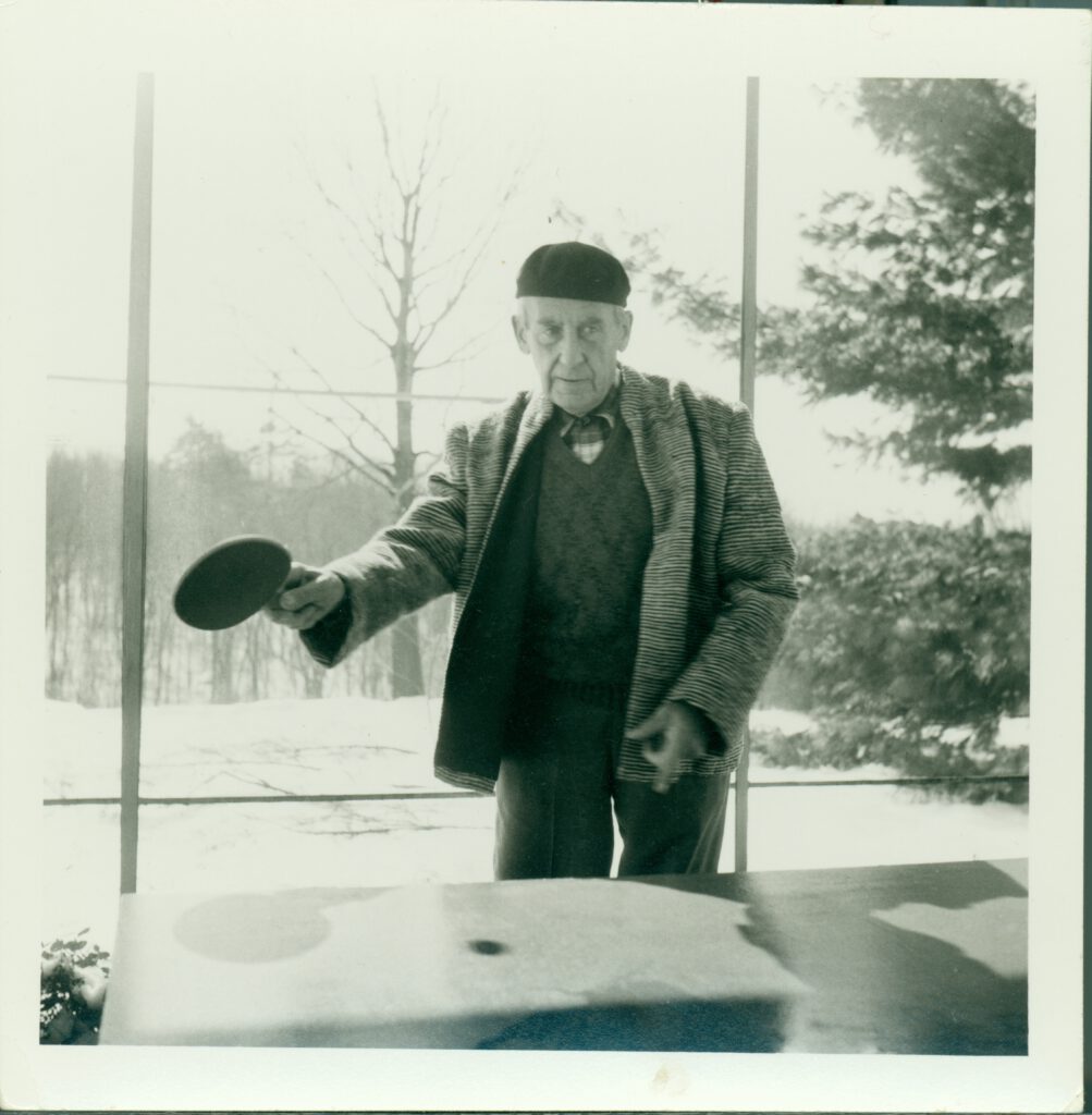 A black and white photo of Walter Gropius playing ping pong.
