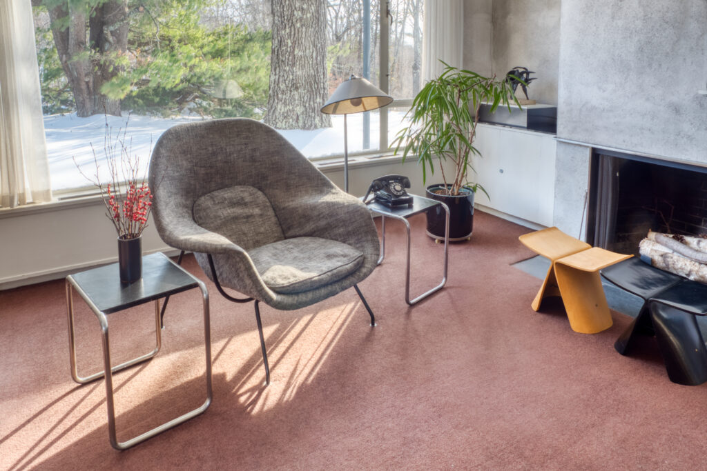 A photo showing the corner of the living room in Gropius House showing end tables and a chair in front of a large window.