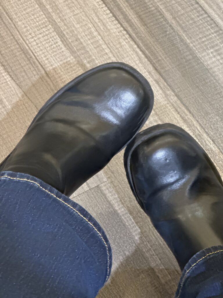 A photo of the bottom of jeans over black boots. The boots are hovering over a wood floor.
