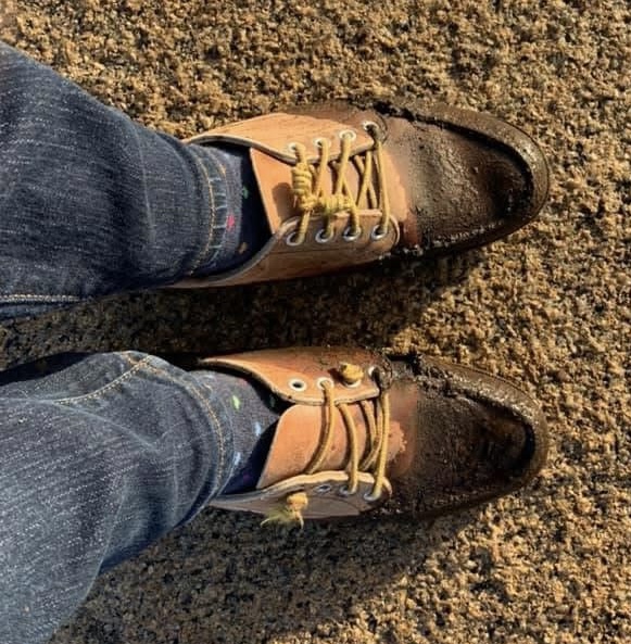 A photo of L.L. Bean leather moccasins. The laces seem frayed and are not laced all the way up. The front of the moccasins are covered in mud.