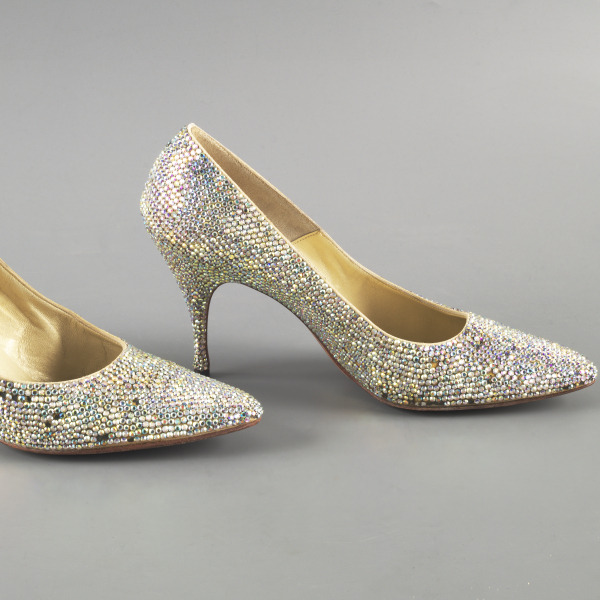 Un par de zapatos cerrados de tacón con pedrería reluciente. La pedrería centellea con múltiples colores al reflejar la luz.