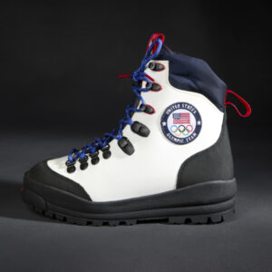 Side profile of a high-top performance sport boot made of white leather with a round U.S.A. & Olympic logo on the side, with black, blue, and red, canvas accents, blue round laces, and thick black, rubber sole.