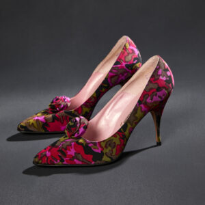 A pair of stiletto high heels with fabric covering in greens, black, and pinks with a fabric rose and very pointed toe sit side by side.