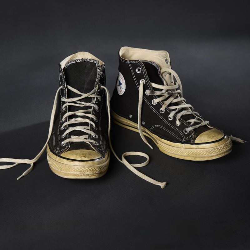 A pair of well used high top black canvas sneakers with white laces and white rubber sole.