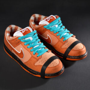 A pair of multi-tone orange suede and leather sneakers with large Nike swoop on side, orange and white picnic table print interior, and black and orange rubber soles, bright blue shoelaces, and a rubber lobster claw style band on around the toe.