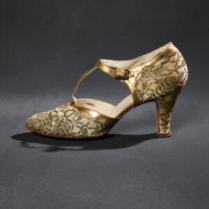 A pair of women’s metallic gold and cream silk brocade high heels with a “t” shaped strap over the instep of the foot.