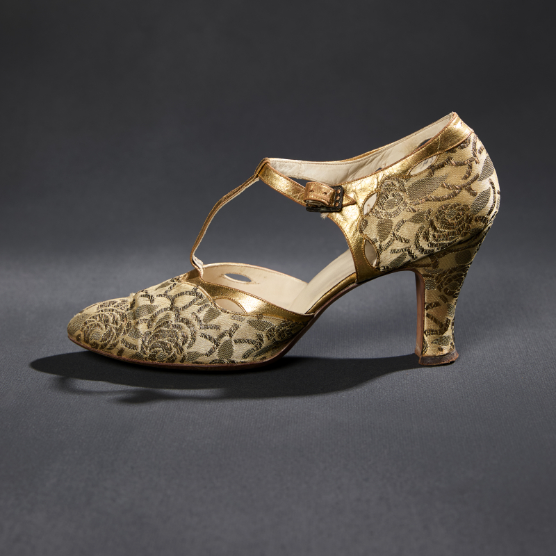 A pair of women’s metallic gold and cream silk brocade high heels with a “t” shaped strap over the instep of the foot.