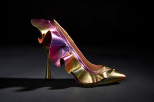 A pair of iridescent leather high heel pumps with a large leather ruffle on the outer edge.