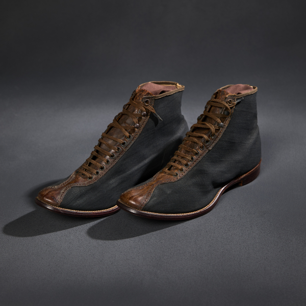 A pair of black cycling shoes with a stripe of brown leather up the front with brown laces fed through a series of holes. The brown sole extends slightly beyond the footprint of the upper shoe.