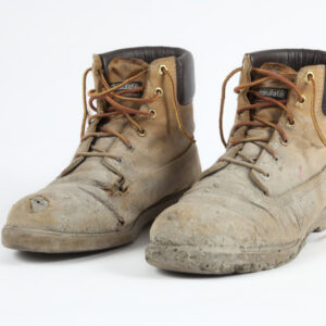 A pair of worn men’s construction boots, with tan leather uppers, tan shoelaces, and black leather ankle padding
