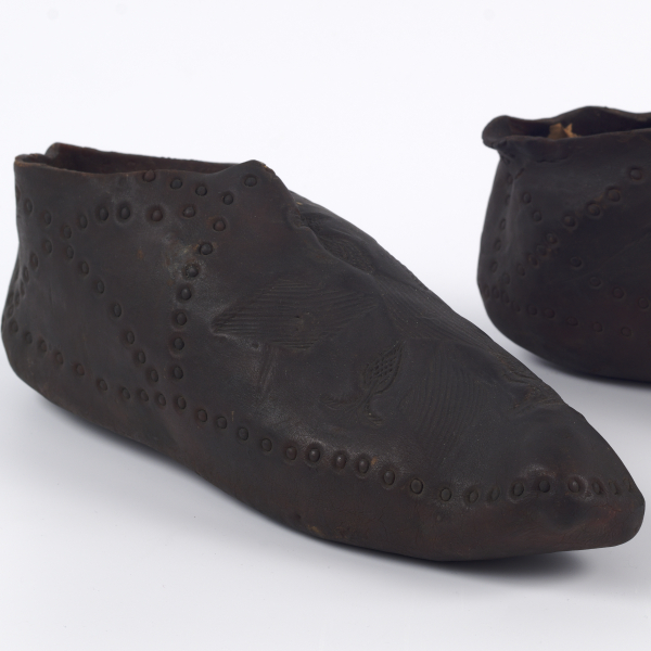 A pair of shaped black rubber slip-on shoes with no visible fastenings. The rubber is impressed with decorative lines of small circles.