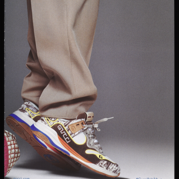 A magazine ad for Gucci, showing a model's lower legs in baggy slacks as they stand on tip-toe in multicolored sneakers.