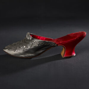 A single mule shoe with a silver-gray silk toe and a red silk inner sole and heel. The front of the shoe features silver-black beadwork.