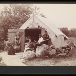 A group of five people sit and stand in front of a semi-permanent tent with a wooden door, some holding bows and arrows. A sign on the tent reads, "Fancy baskets, bows, arrows, and canoes for sale here."