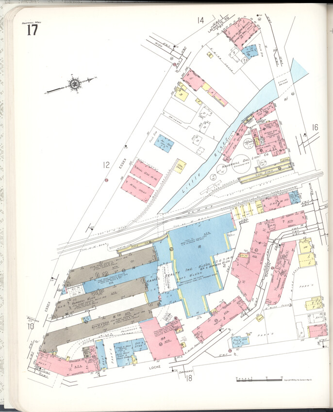 A map showing the triangular area between Essex Street, Winter Street, and Locke Street. The railroad tracks divide the image at center, with surrounding brick, wood, and concrete buildings visible. The three brown-gray (fireproof) buildings at bottom left are enmeshed with a large blue area (concrete construction) of loft buildings.