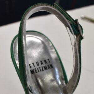 A close-up of the back heel strap of a green heel with plastic Vivak support.