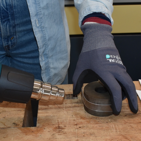 A gloved hand shapes a piece of plastic around a mold in front of a heat gun.