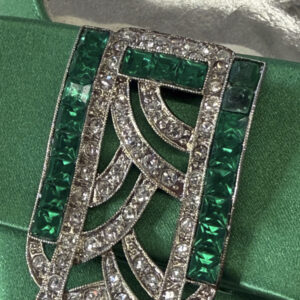 A close up of a silver brooch set with green and white rhinestones.