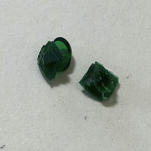 A close-up of two irregularly shaped green epoxy rhinestones on a white background.