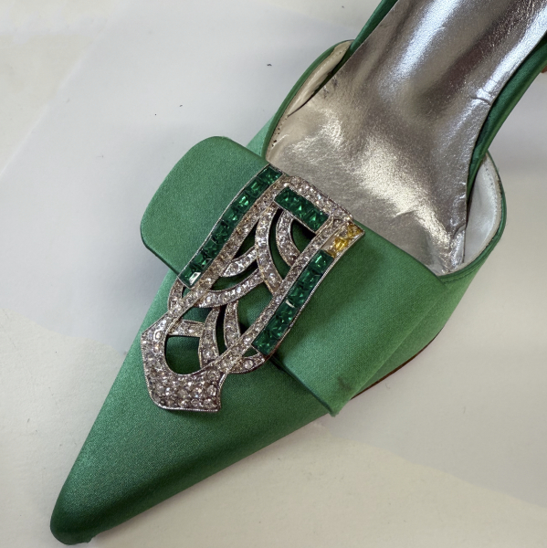 A green heel with pointed toe embellished with a silver brooch set with green and white rhinestones. Two rhinestones are missing.