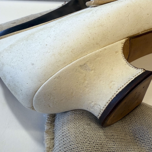 A detail image of the heel of a white leather heeled shoe. The leather looks complete, with a small difference in color between one particular patch.