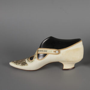 A pair of white leather heels with decorative beadwork. The leather shoe on the left in the picture is darker than the one on the right.