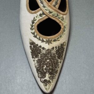 A detail image of the top of a white leather shoe with decorative beadwork. The left side of the shoe is noticeably lighter than the right side of the shoe.