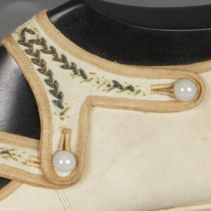 A detail image of the attachment point between a white leather strap decorated with beadwork and the side of a white leather shoe. The threads on the beadwork are broken in places and, in some places, have been tacked down.