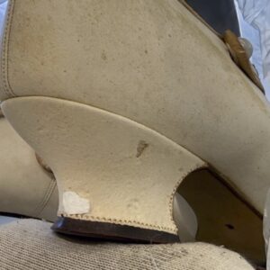 A detail image of the heel of a white leather heeled shoe. There is a piece of leather missing from the side of the heel.
