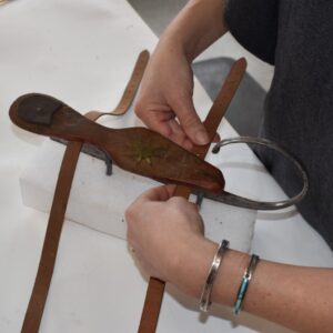 A conservator’s hands place new leather straps underneath the wooden platform of the skate.