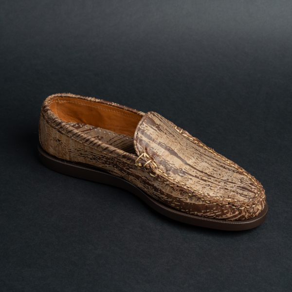 A man's left shoe with a wood-grain-like brown and beige texture and visible light stitching.