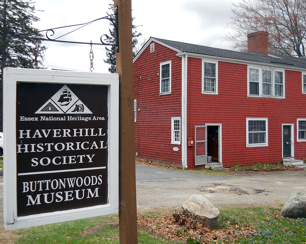 The exterior of the Haverhill Historical Society's Buttonwoods Museum. The museum is a red, two-floor wooden building with a chimey.