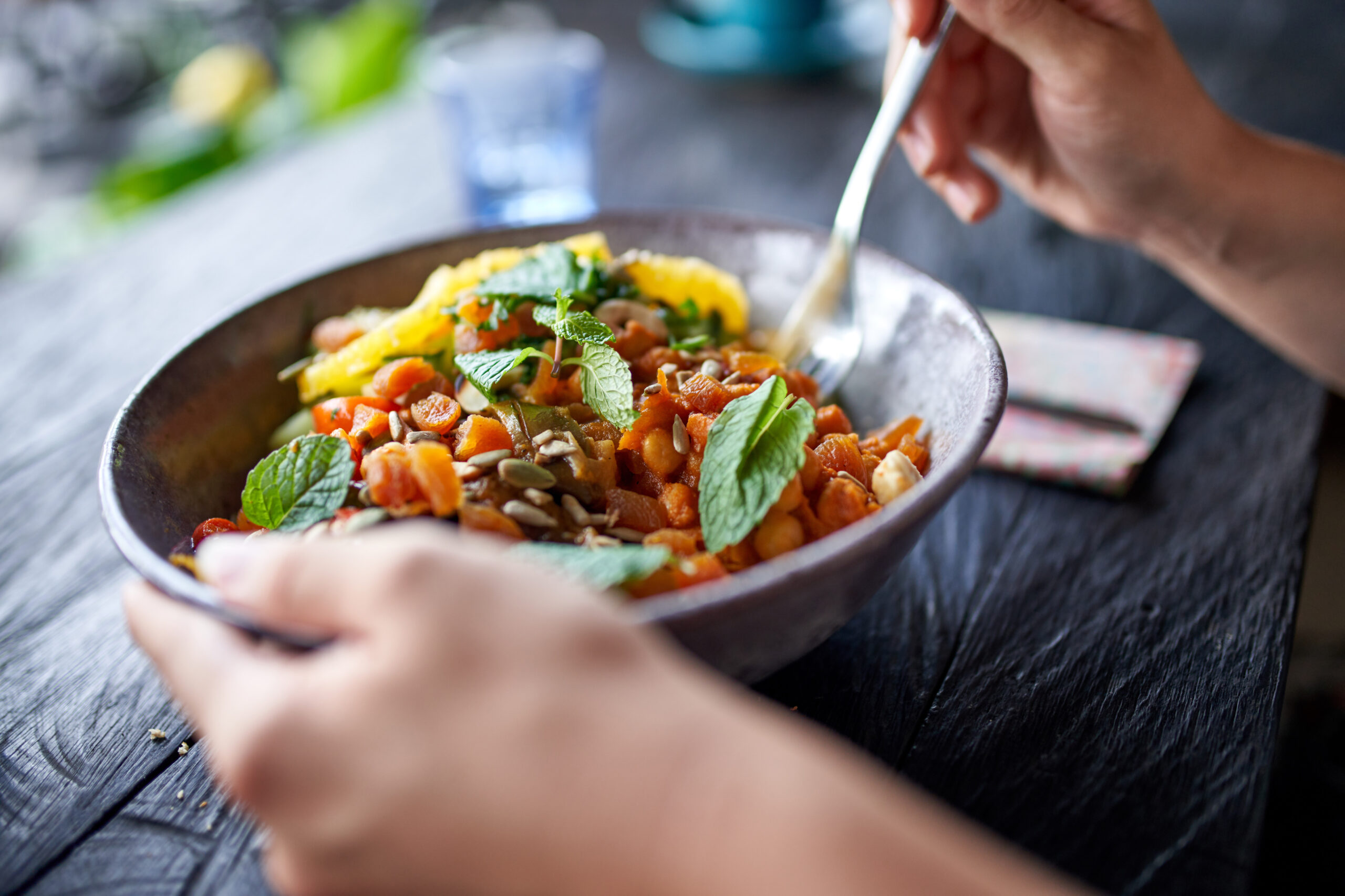 A photo of a bowl on a table flanked by two hands. Herbs and chickpeas are visible in the bowl.