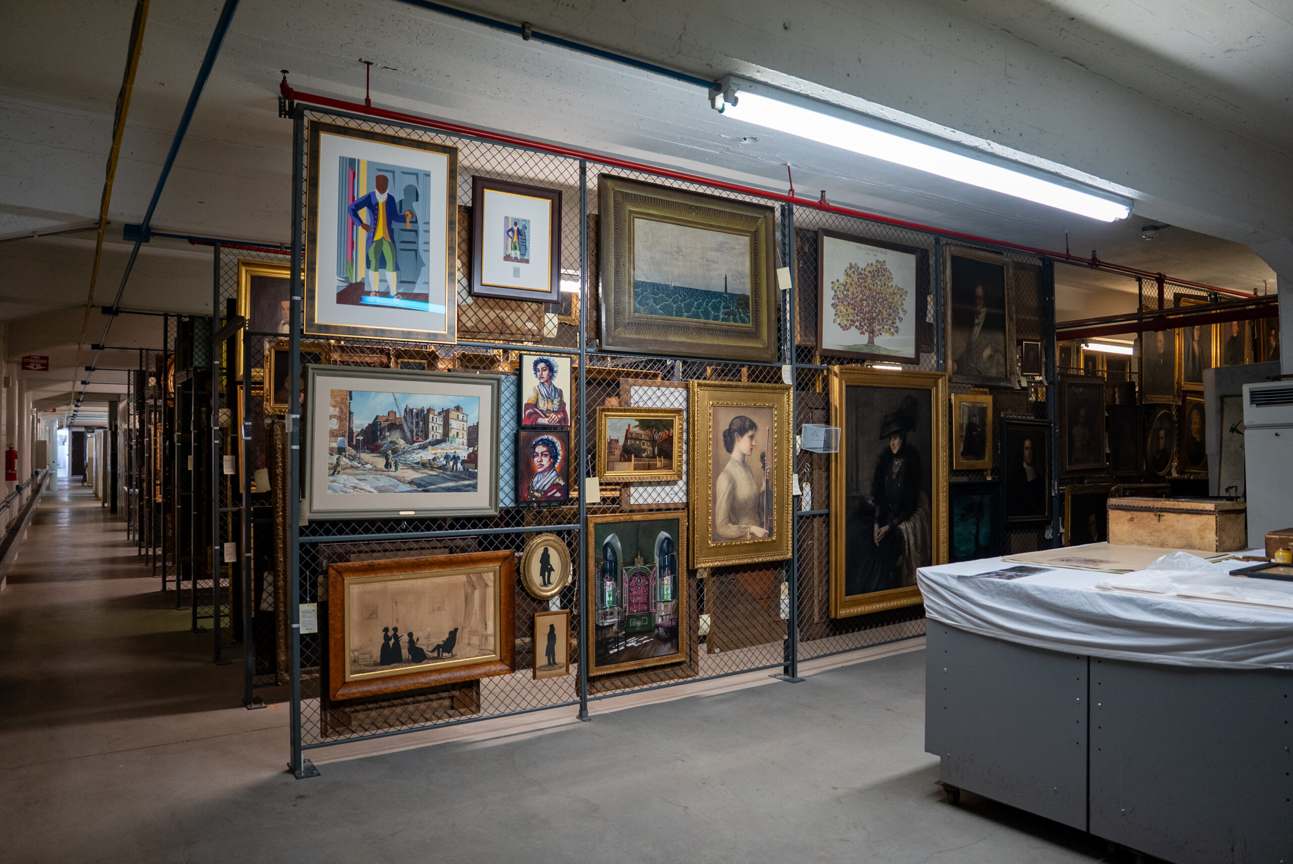 Items in the Historic New England collections including paintings and prints. There is a hallway on the left leading to rows of items in the collections.