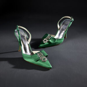 A pair of green satin pumps with pointed toes. Each features a central green satin flap over the toe held in place by a rhinestoned buckle, and green back straps.
