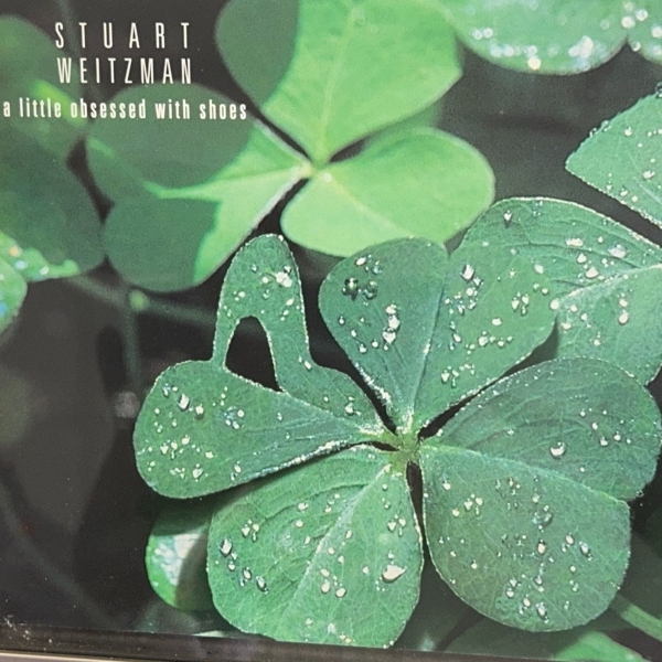 A magazine ad showing several clover leaves, including a four-leaf clover with a shoe-shaped leaf. At top right, "Stuart Weitzman: a little obsessed with shoes."