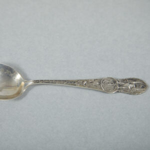 A silver spoon with an elaborately decorated handle. The bowl of the spoon includes “Haverhill, Mass.” and an etching of a high-heeled shoe.