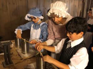 Students in historical costume making dip candles.