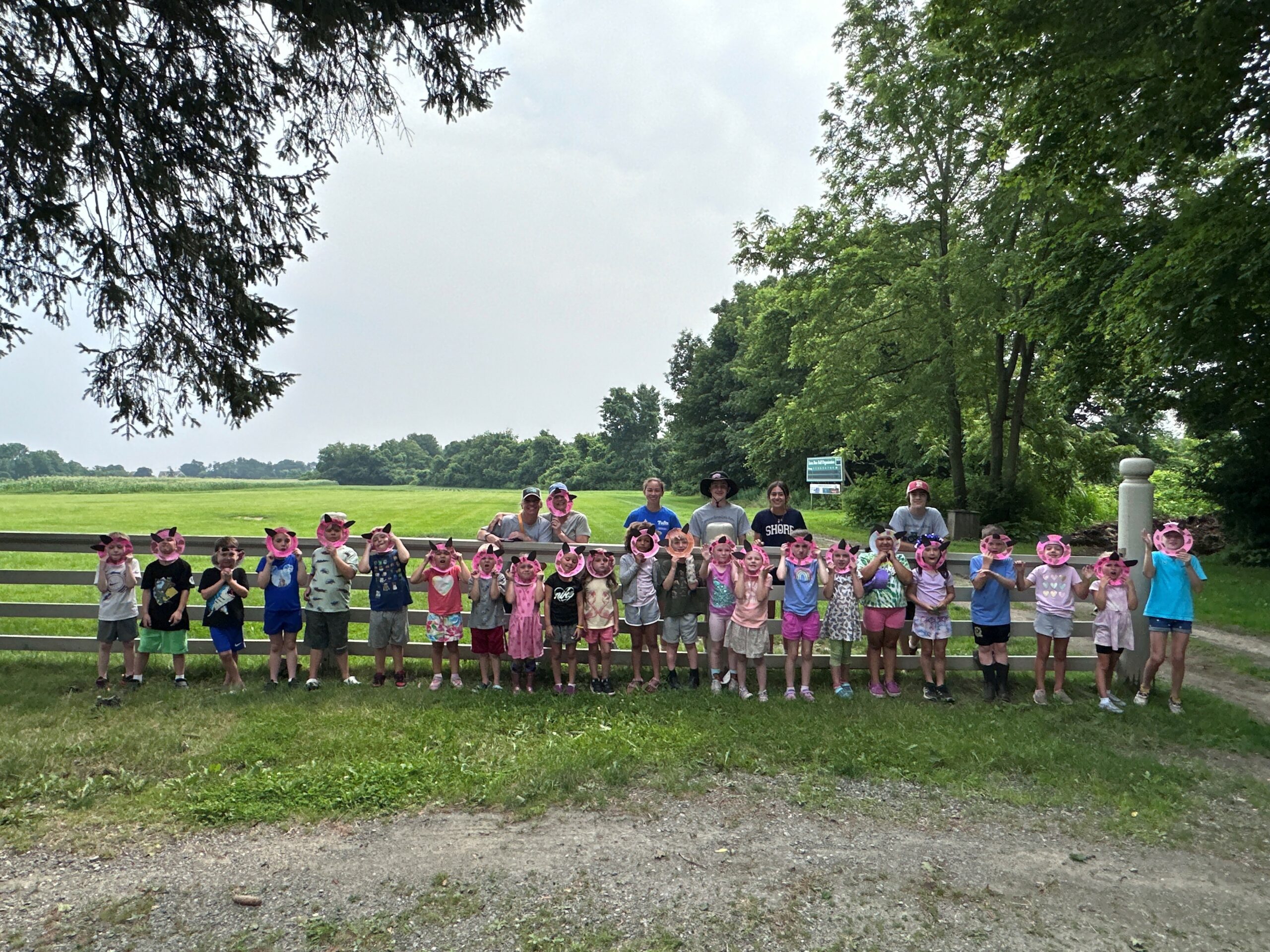 Campers pose with pig masks in front of a field.