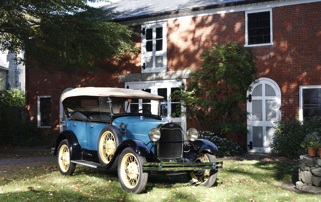 Blue 1929 Model A Ford in front of brick carriage barn