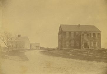 Exterior view of the Rocky Hill Meeting House and Parsonage, Amesbury, Mass. Two men are gatehred near the front doorway.
