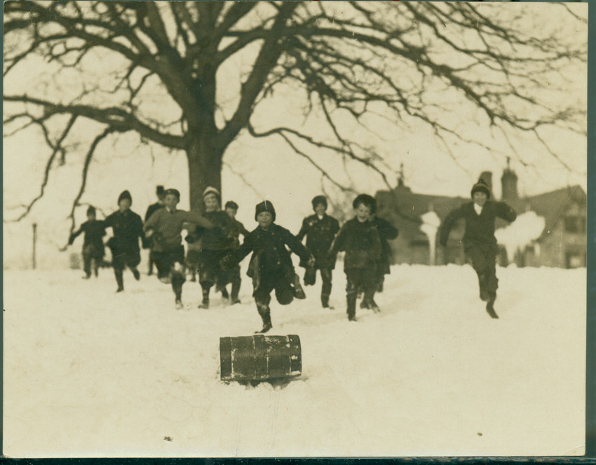 Children run after a toboggan sliding down a slope