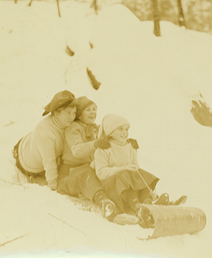 Three girls ride a toboggan