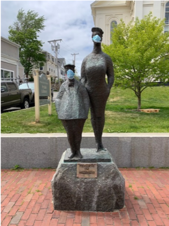 Two face masks adorn a statue of two people in a town square.