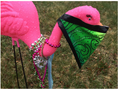 A plastic lawn flamingo wears a green face mask.