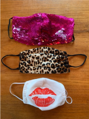 Three protective face masks -- one with pink sequins, one with cheetah print, and one with a kiss mark -- sit on a table.