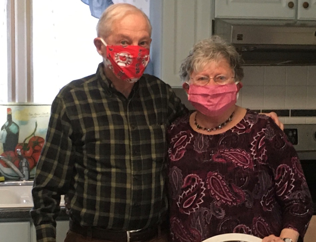 Two people stand in a kitchen wearing protective face masks.