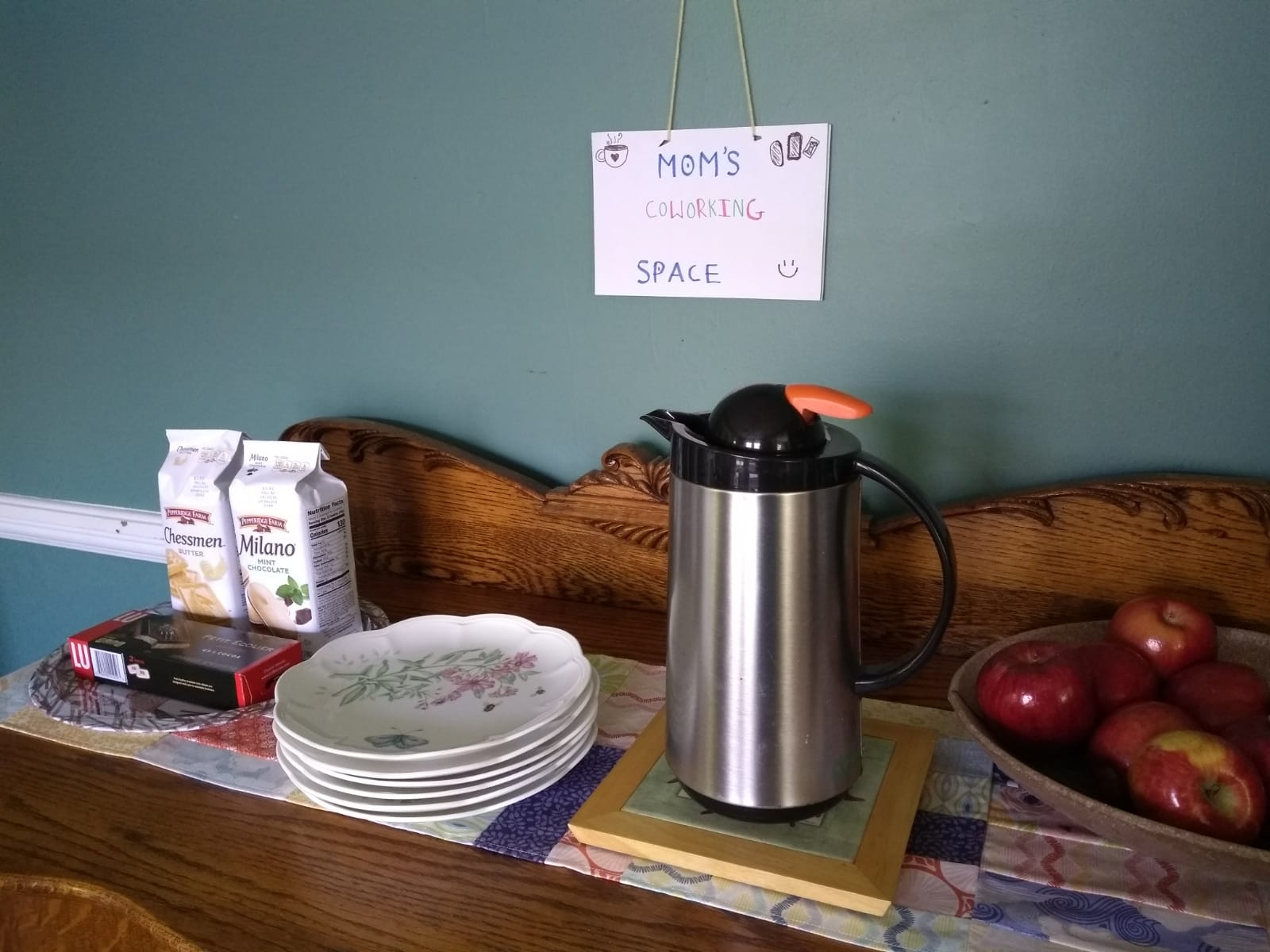Plates, cookies, and coffee pot underneath sign reading, "Mom's Coworking Space"